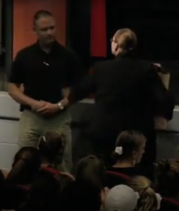 A speaker addresses an audience in a dimly lit room.